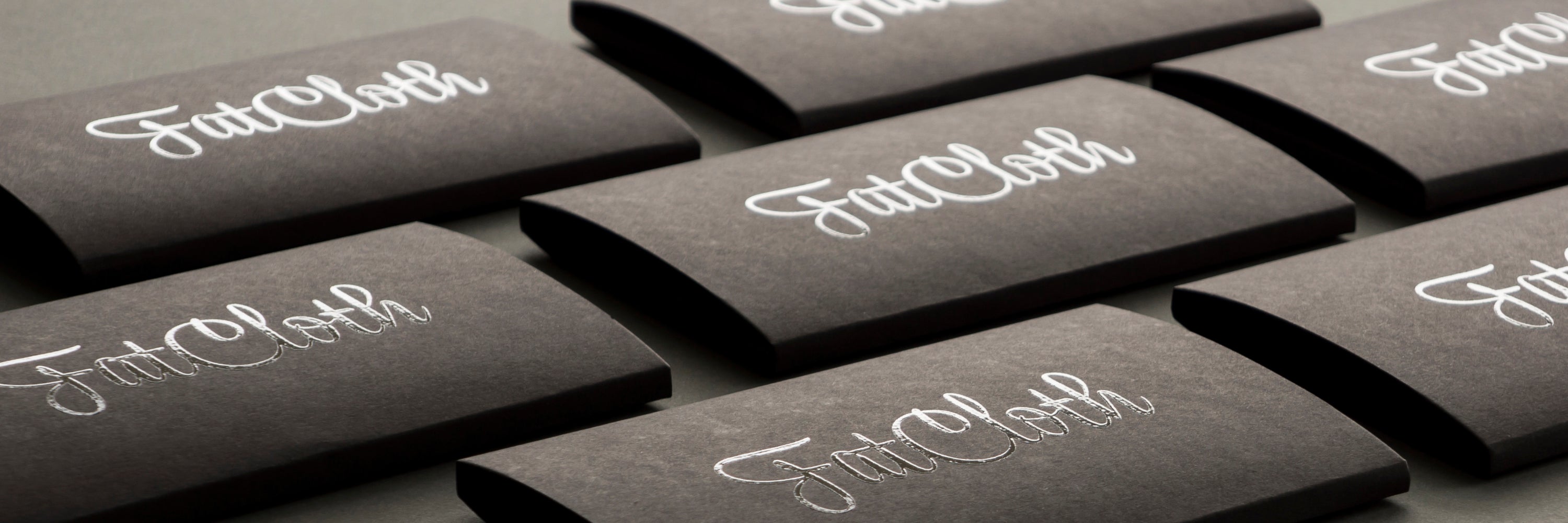Black FatCloth product boxes with light reflecting logos tiled up on a gray background
