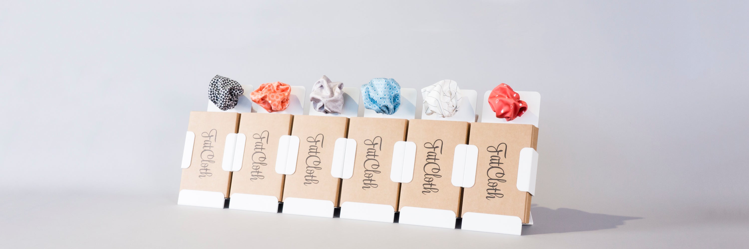 Six FatCloth product displayswith colorful pocket squares in row on light gray background