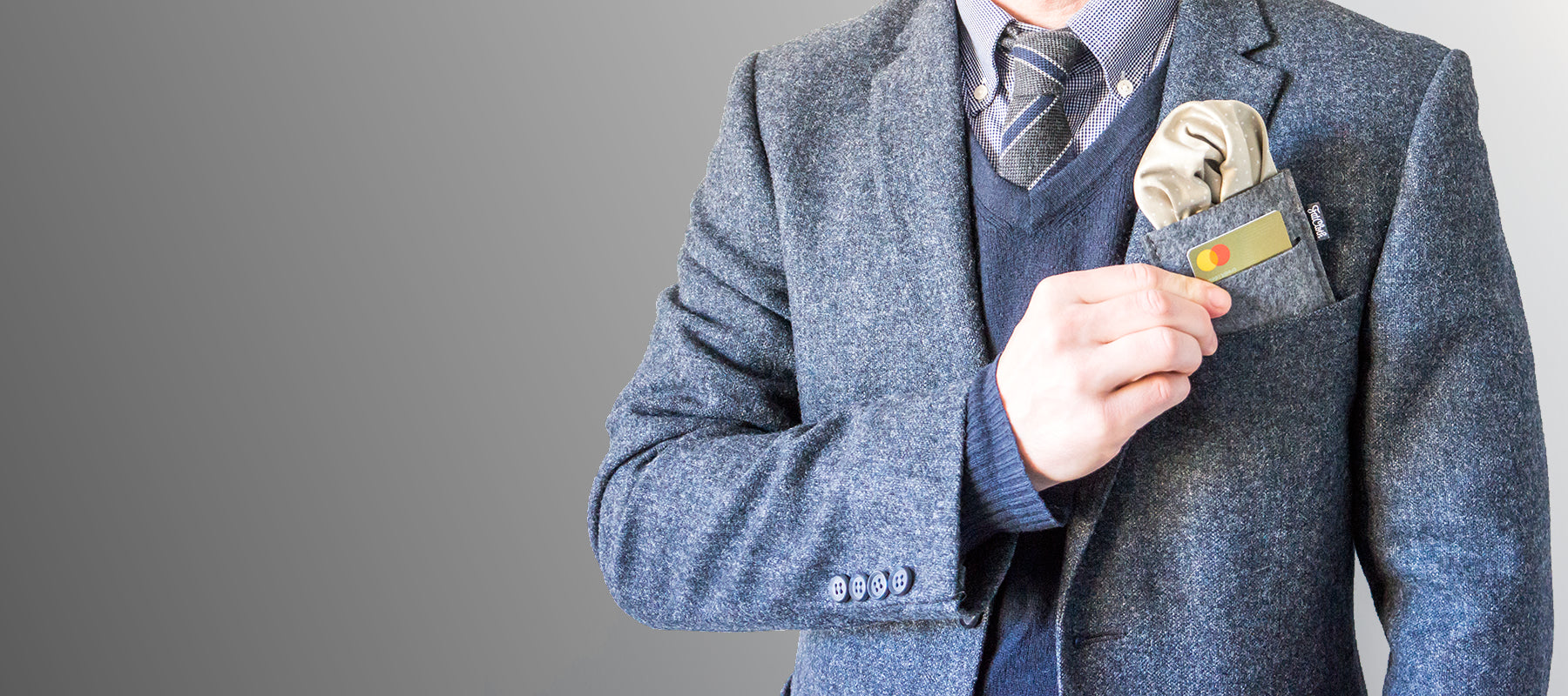 Cropped torso of a man in gray woolen blazer holding a pocket square holder in right hand, gray background