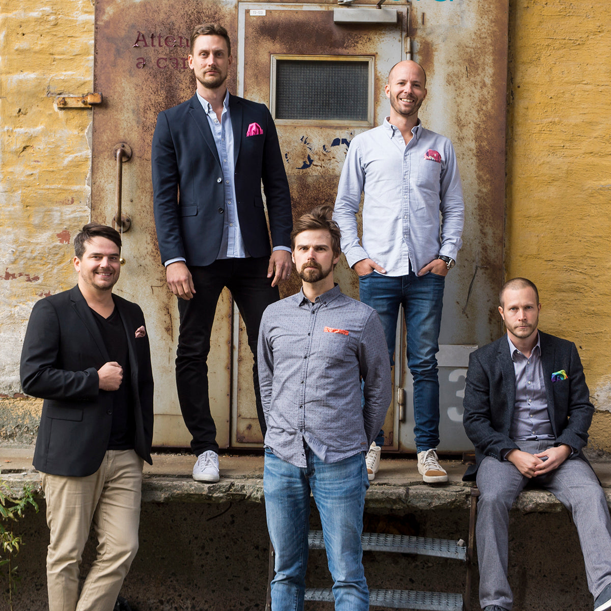 Five men wearing colourful pocket squares in front of an industrial loading dock