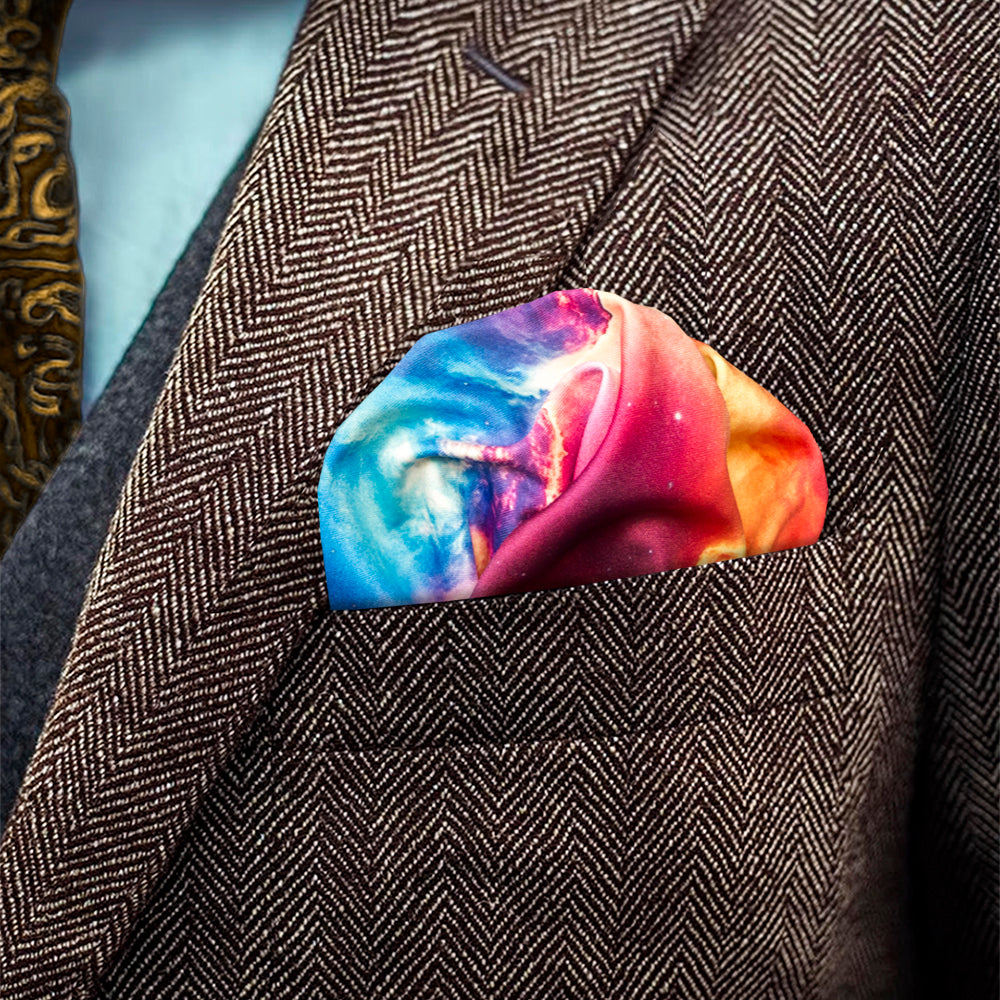 A close-up of a multicolor galaxy-print pocket square tucked into a brown herringbone suit jacket.