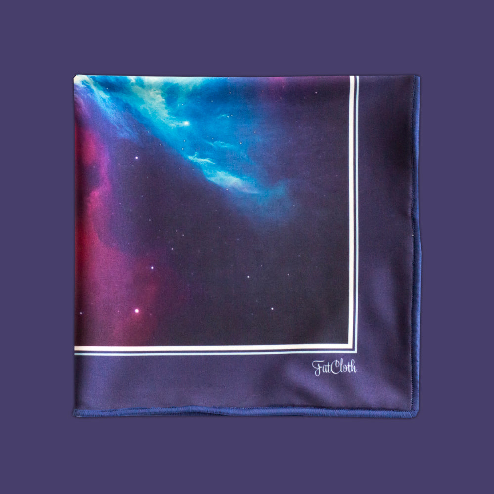 A multipurpose pocket square with a galaxy print, featuring a dark space design with blue, purple, and pink nebulae, bordered by white lines and the brand name 'FatCloth' in white script, set against a solid dark purple background.
