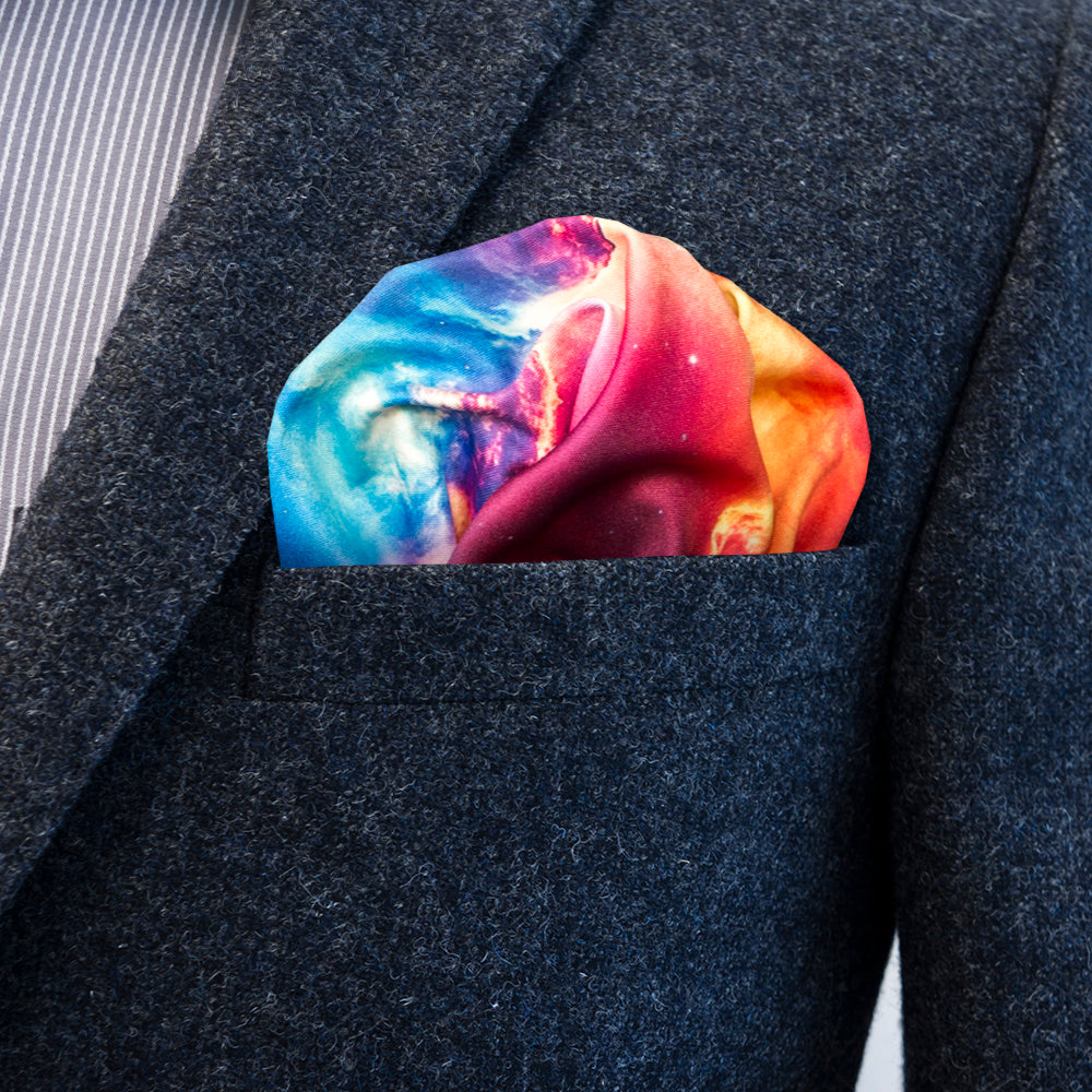 A close-up of a dark charcoal gray suit jacket with a vibrant, multicolored galaxy print pocket square tucked into the chest pocket.